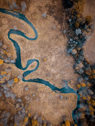 An aerial shot of a river in the middle of a dry grassy field with trees great for background or a blog